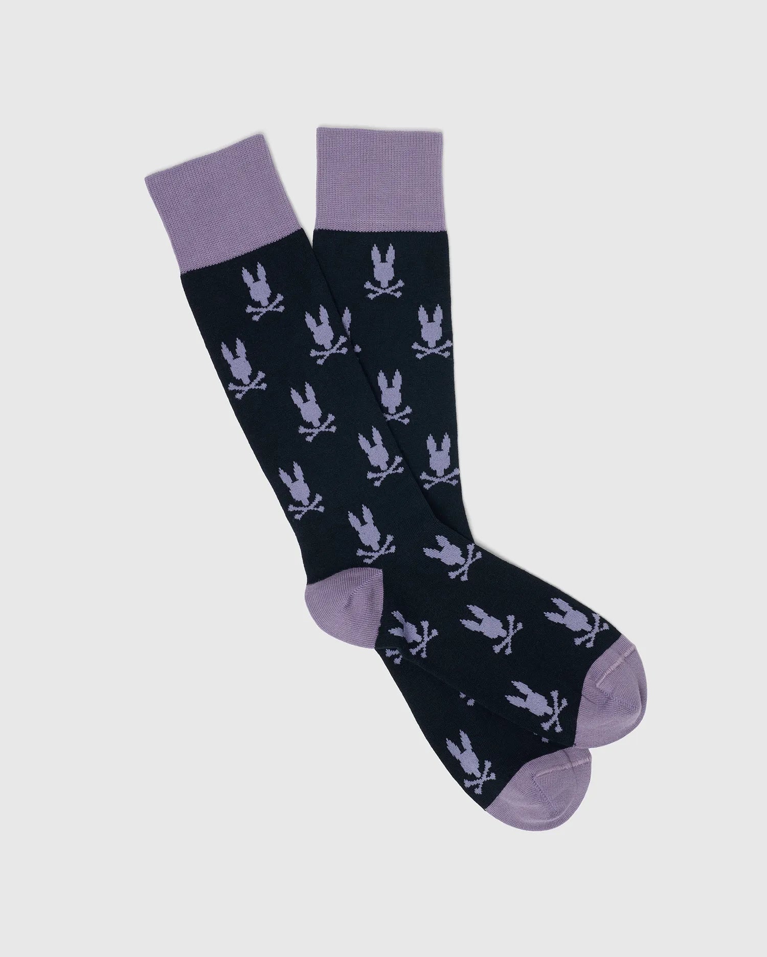 Psycho Bunny's MENS ALL OVER BUNNY DRESS SOCK - B6F750F200 features black knee-high socks with purple cuffs, heels, and toes made from soft Pima cotton. With a pattern of crossed bones and an eagle motif in purple on a light gray background, these socks offer both comfort and style.