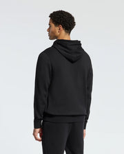 Rewrite: A person with curly hair is standing in the stylish black MENS PIERCE ESSENTIAL FRENCH TERRY HOODIE by Psycho Bunny, along with matching pants, facing away from against a plain background.