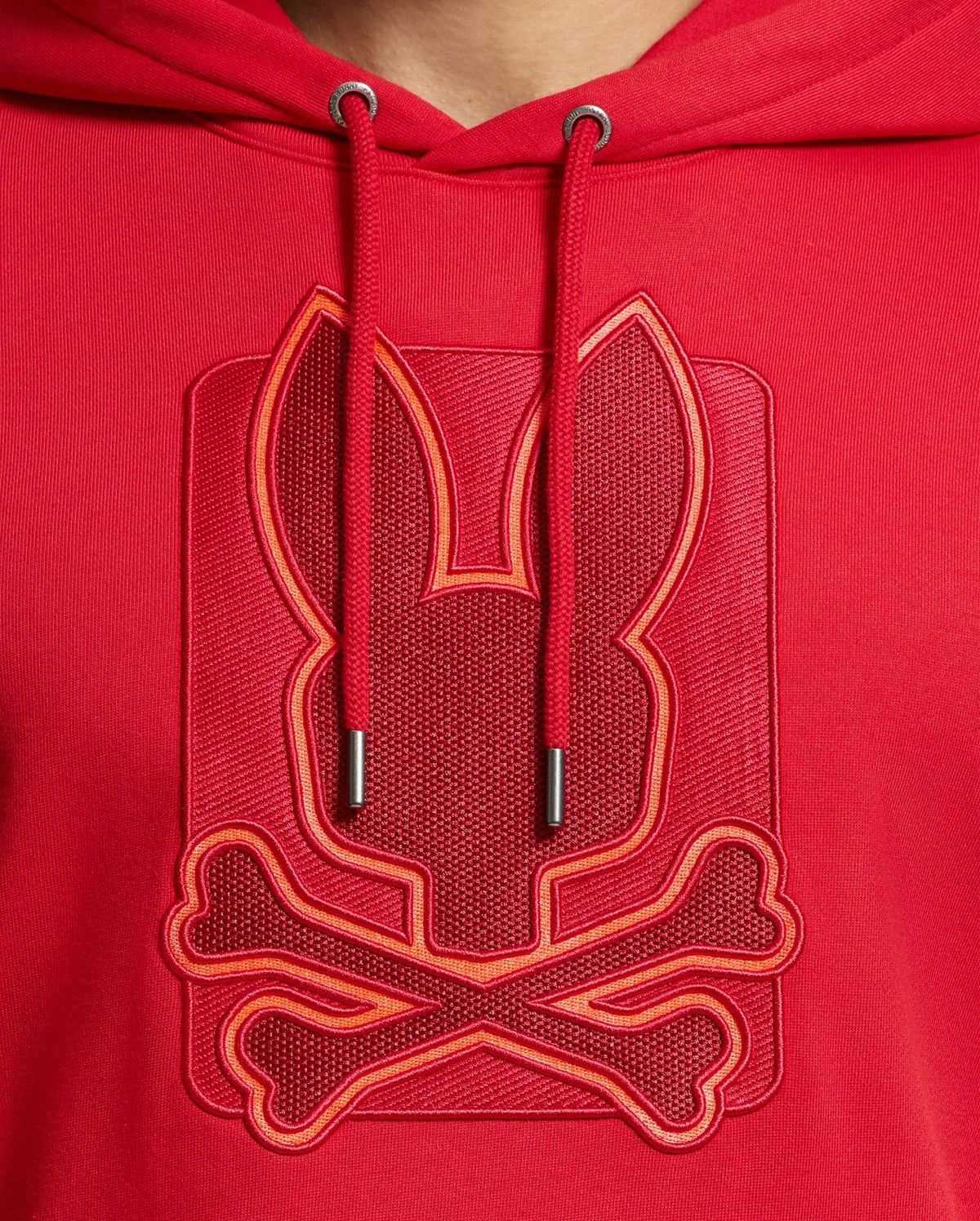 Close-up of the MENS PIERCE ESSENTIAL FRENCH TERRY HOODIE by Psycho Bunny, crafted in high-quality cotton and featuring a stylish embroidered design of a stylized rabbit head and crossbones. The embroidery logo is embossed and outlined with brighter red thread, providing a bold contrast on the fabric.