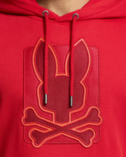 Close-up of the MENS PIERCE ESSENTIAL FRENCH TERRY HOODIE by Psycho Bunny, crafted in high-quality cotton and featuring a stylish embroidered design of a stylized rabbit head and crossbones. The embroidery logo is embossed and outlined with brighter red thread, providing a bold contrast on the fabric.