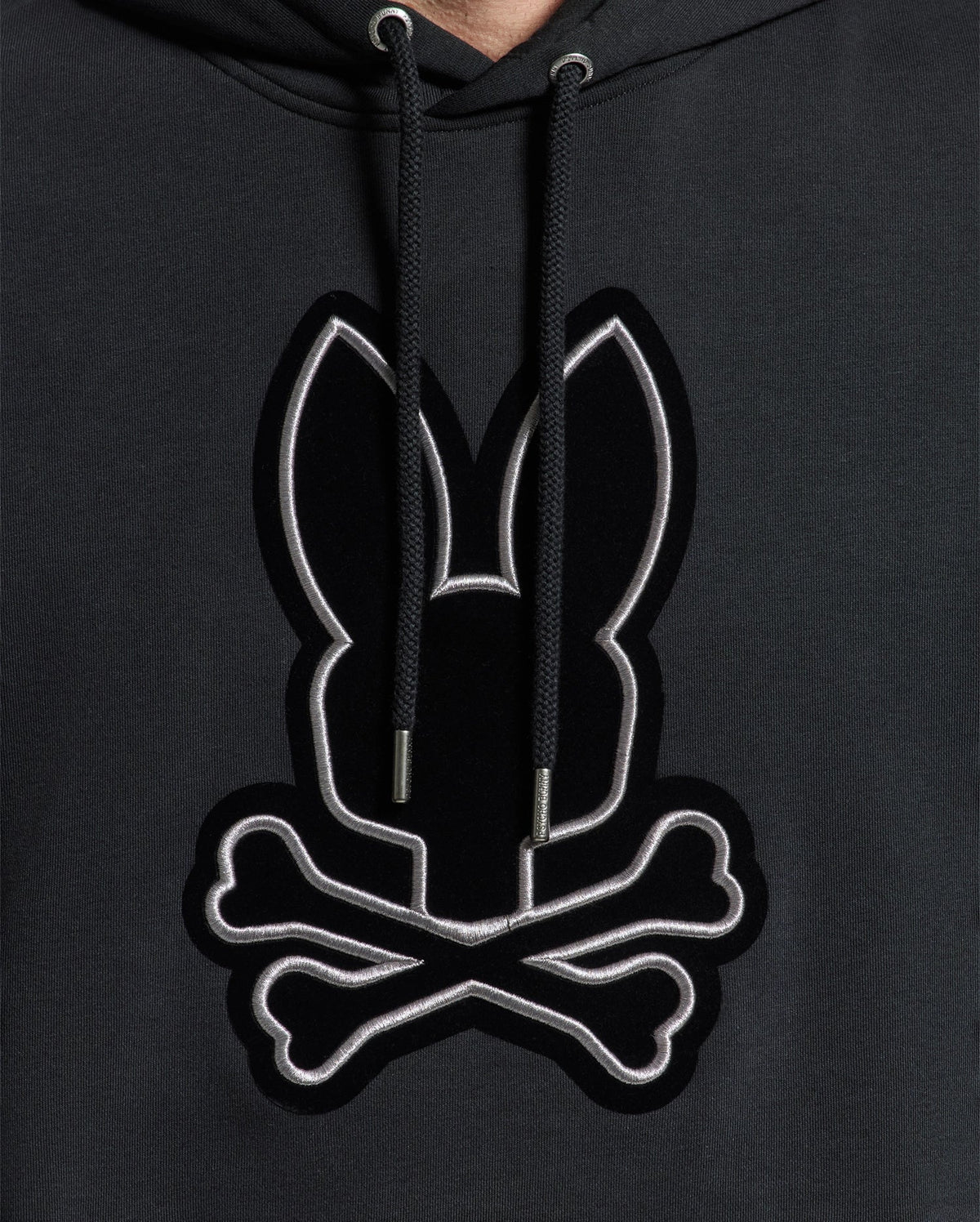 A close-up of the Psycho Bunny MENS ALEXANDER HOODIE - B6H154E200 showcases a chest logo featuring a stylized black bunny and crossed bones outlined in white. This comfortable men’s hoodie comes with drawstrings for an adjustable fit.