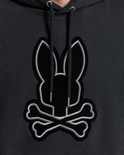 A close-up of the Psycho Bunny MENS ALEXANDER HOODIE - B6H154E200 showcases a chest logo featuring a stylized black bunny and crossed bones outlined in white. This comfortable men’s hoodie comes with drawstrings for an adjustable fit.
