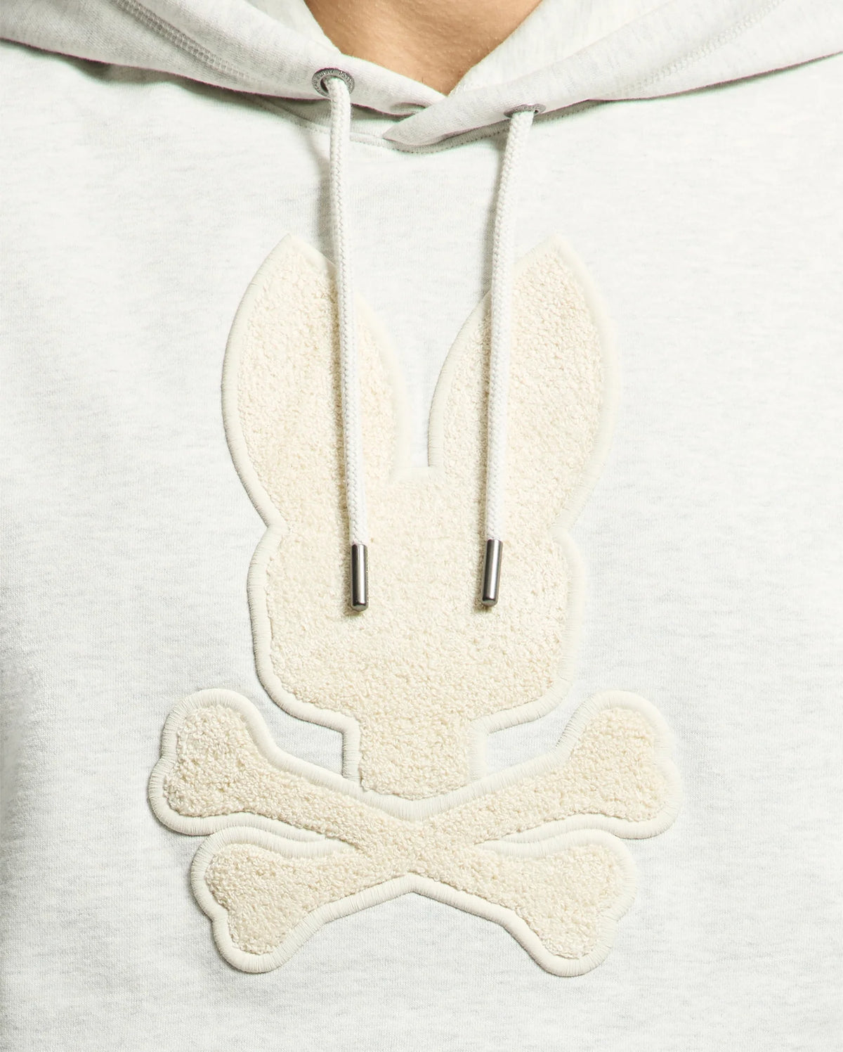 The Psycho Bunny MENS ELDORADO BRUSH BACK HOODIE (B6H234E200) features a gray applique of a stylized bunny head with long ears over crossed bones, reminiscent of a pirate flag. Its brush-back design offers comfort and a textured monochrome look, perfect for swaddle season.