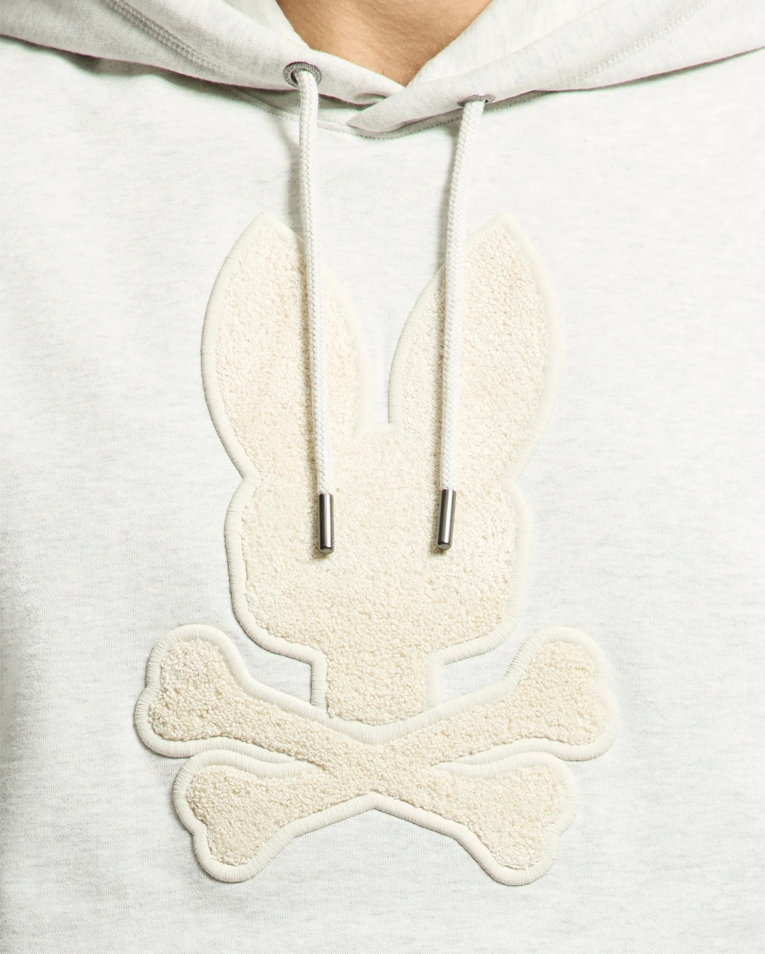The Psycho Bunny MENS ELDORADO BRUSH BACK HOODIE (B6H234E200) features a gray applique of a stylized bunny head with long ears over crossed bones, reminiscent of a pirate flag. Its brush-back design offers comfort and a textured monochrome look, perfect for swaddle season.
