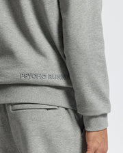 Dressed for swaddle season, a person wears the gray MENS ELDORADO BRUSH BACK HOODIE by Psycho Bunny, made from cozy brush-back cotton. Paired with matching gray pants, only their side and back are visible.