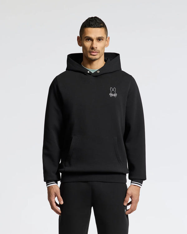 A person in a Psycho Bunny MENS DACANO PERFORATED HOODIE - B6H239E200, featuring a breathable design and embroidered bunny logo on the chest, stands against a plain white background. They have short dark hair and look directly at the camera with hands by their sides.