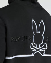 Close-up of the back of a Psycho Bunny MENS DACANO PERFORATED HOODIE in black, showcasing an embroidered bunny skull and crossbones logo with "PSYCHO BUN" text in white. It features breathable, perforated texture and a horizontal white trim below the logo.