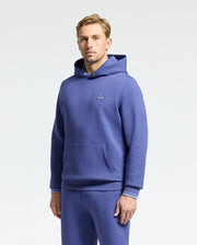 A person in a matching blue Psycho Bunny Dacano perforated stretch cotton-blend jersey hoodie and sweatpants stands against a plain background. The hoodie, B6H239E200, features a small embroidered logo on the chest.