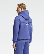 A person wearing the Psycho Bunny Mens Dacano Perforated Hoodie (B6H239E200) and matching pants stands against a white background; the hoodie back displays "Psycho Bunny" and an embroidered bunny and bones logo on comfortable stretch cotton-blend jersey.