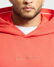 A person wearing the Men's Nora Classic French Terry Hoodie in coral from Psycho Bunny, featuring an embroidered wordmark. The hoodie, crafted from soft French terry fabric, includes a white hood lining. The background is plain white.
