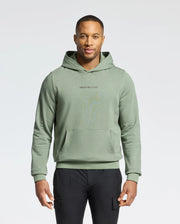 A man poses against a white backdrop in a Psycho Bunny light green MENS NORA CLASSIC FRENCH TERRY HOODIE - B6H434F200 with an embroidered logo. He pairs it with black pants, his short hair enhancing the simple scene.