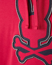 Zoomed-in view of the red MENS WALTER LIGHTWEIGHT HOODIE - B6H476D200 by Psycho Bunny, crafted from Micro French Terry. It displays a stitched design of a stylized rabbit with crossed bones beneath it, using black and white thread. The texture of the fabric and the intricate 3D outlined embroidery stand out clearly.