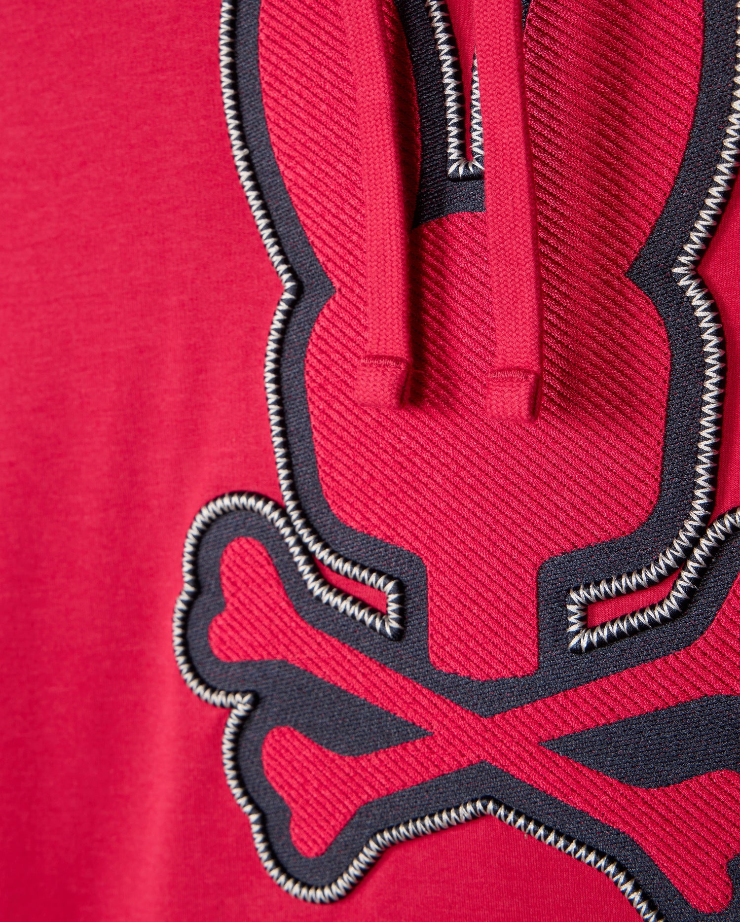Zoomed-in view of the red MENS WALTER LIGHTWEIGHT HOODIE - B6H476D200 by Psycho Bunny, crafted from Micro French Terry. It displays a stitched design of a stylized rabbit with crossed bones beneath it, using black and white thread. The texture of the fabric and the intricate 3D outlined embroidery stand out clearly.