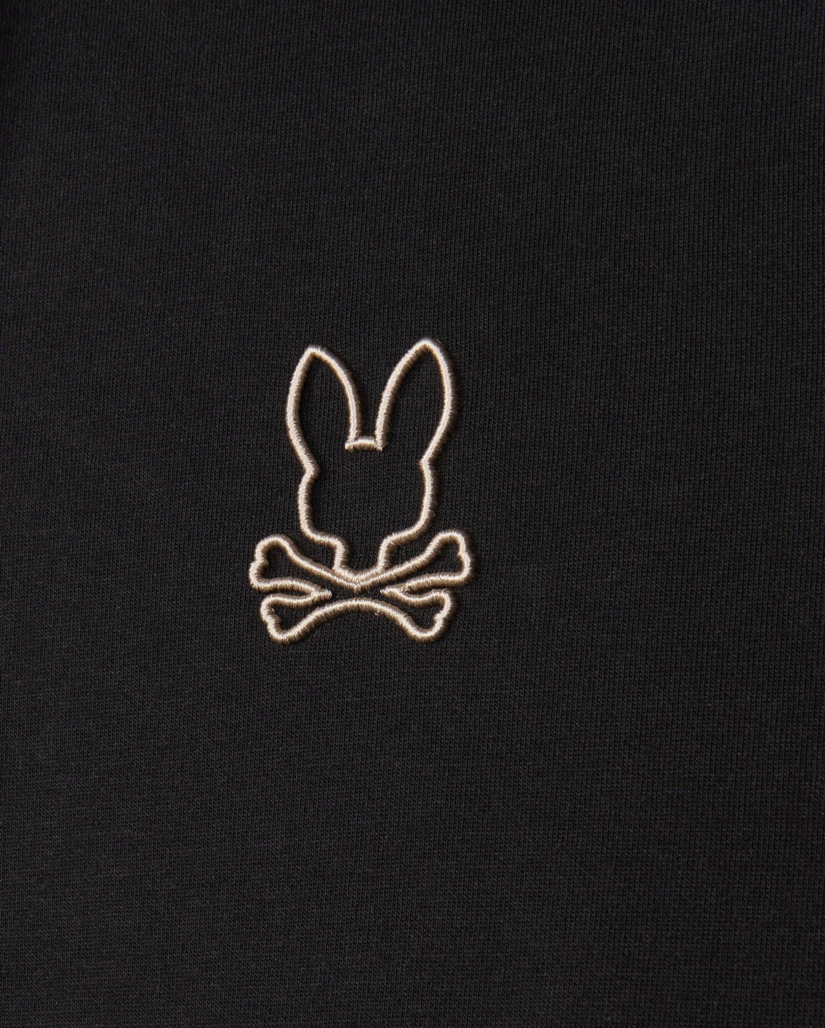 Close-up of the Psycho Bunny MENS JAMES PREMIUM HOODIE - B6H789D200, showcasing an embroidered design in white thread on its premium jersey fabric. The design features a silhouette of rabbit ears above crossbones, delivering a playful and slightly edgy visual. The embroidery is centered in the image.