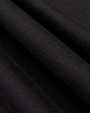 A close-up view of the smooth, black fabric from the Psycho Bunny MENS JAMES PREMIUM HOODIE - B6H789D200 reveals three parallel folds running diagonally across the image. The texture appears soft and even, resembling essential fleece, with a matte finish that creates a subtle interplay of light and shadow on the surface.