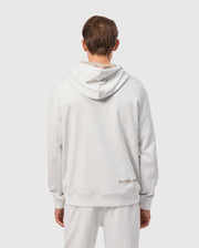 A person is shown from the back wearing the MENS JAMES PREMIUM HOODIE - B6H789D200 by Psycho Bunny in light gray, paired with matching pants. This premium jersey hoodie is adorned with an embroidered bunny near the bottom, adding a touch of stylish warmth. The background is plain and light-colored.