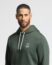 A man with short hair and a beard is wearing the trendy MENS JAMES PREMIUM HOODIE - B6H789D200 by Psycho Bunny, featuring its signature small stylized rabbit logo on the chest. This lightweight green hoodie for men includes white drawstrings, set against a plain, light-colored background.