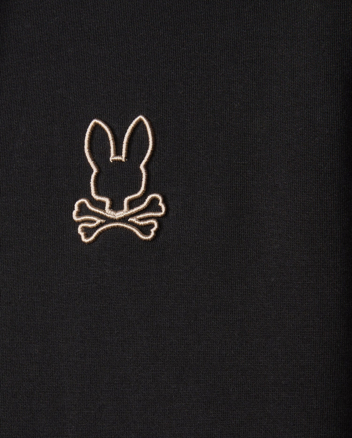 The MENS JAMES PREMIUM ZIP HOODIE - B6H793D200 by Psycho Bunny is a black zip-up hoodie featuring an embroidered Bunny graphic of a stylized bunny head above crossed bones, resembling a skull and crossbones motif. The design is outlined in light-colored thread on double-faced premium jersey.