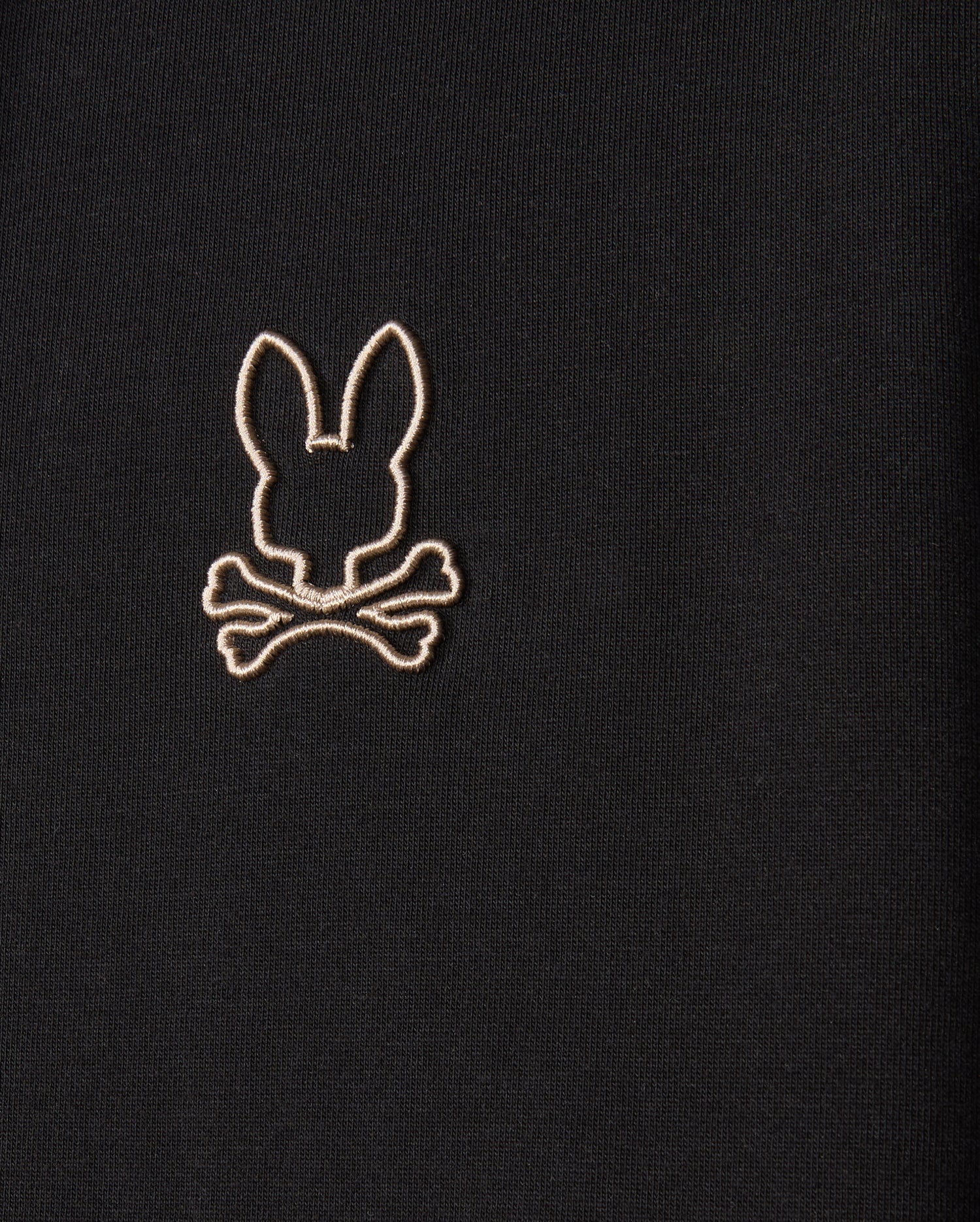 The MENS JAMES PREMIUM ZIP HOODIE - B6H793D200 by Psycho Bunny is a black zip-up hoodie featuring an embroidered Bunny graphic of a stylized bunny head above crossed bones, resembling a skull and crossbones motif. The design is outlined in light-colored thread on double-faced premium jersey.