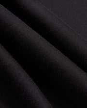 Close-up of the black fabric from the MENS JAMES PREMIUM ZIP HOODIE - B6H793D200 by Psycho Bunny showing its texture. The fabric appears soft and slightly folded, creating gentle shadows and highlights. The material, part of a double-faced premium jersey, looks smooth and uniform in color.