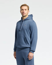 A person wearing the Psycho Bunny MENS LEVY ESSENTIAL FLEECE HOODIE - B6H859D200 in soft, 100% cotton French terry with a small logo on the chest stands against a plain white background, paired with matching blue sweatpants. They have short hair and a neutral expression.