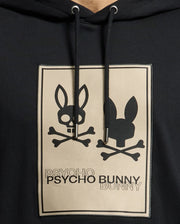 Introducing the **MENS MONROE TWILL PATCH FLEECE HOODIE - B6H926D200** from *Psycho Bunny*. This stylish black hoodie is crafted from French terry fabric and features a unique graphic design of two bunny skulls. One skull showcases ear bones, while the other exhibits shaded ears over crossed bones. The "Psycho Bunny" text seamlessly integrates comfort with an edgy style statement.
