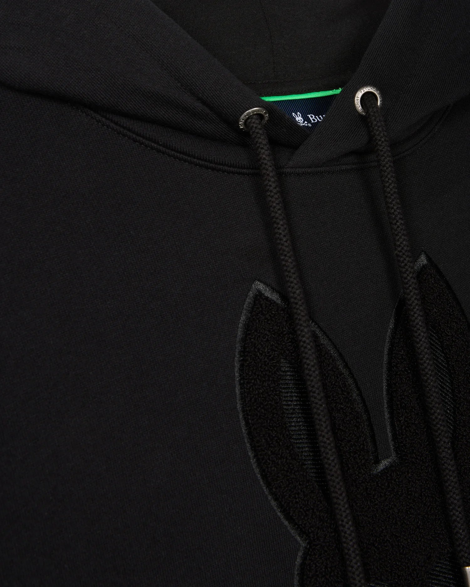 Close-up of a black Psycho Bunny Men's Pacific Chenille Hoodie, model B6H930D200, boasting drawstrings and an adorable furry rabbit ear design. A small hint of the blue tag is visible inside the neckline, adding charm to this cozy piece.