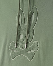 The MENS PACIFIC CHENILLE HOODIE - B6H930D200 by Psycho Bunny features green fabric embellished with chenille embroidery of a stylized bunny skull and crossbones. Cord drawstrings gracefully drape over the design, adding an elegant touch.