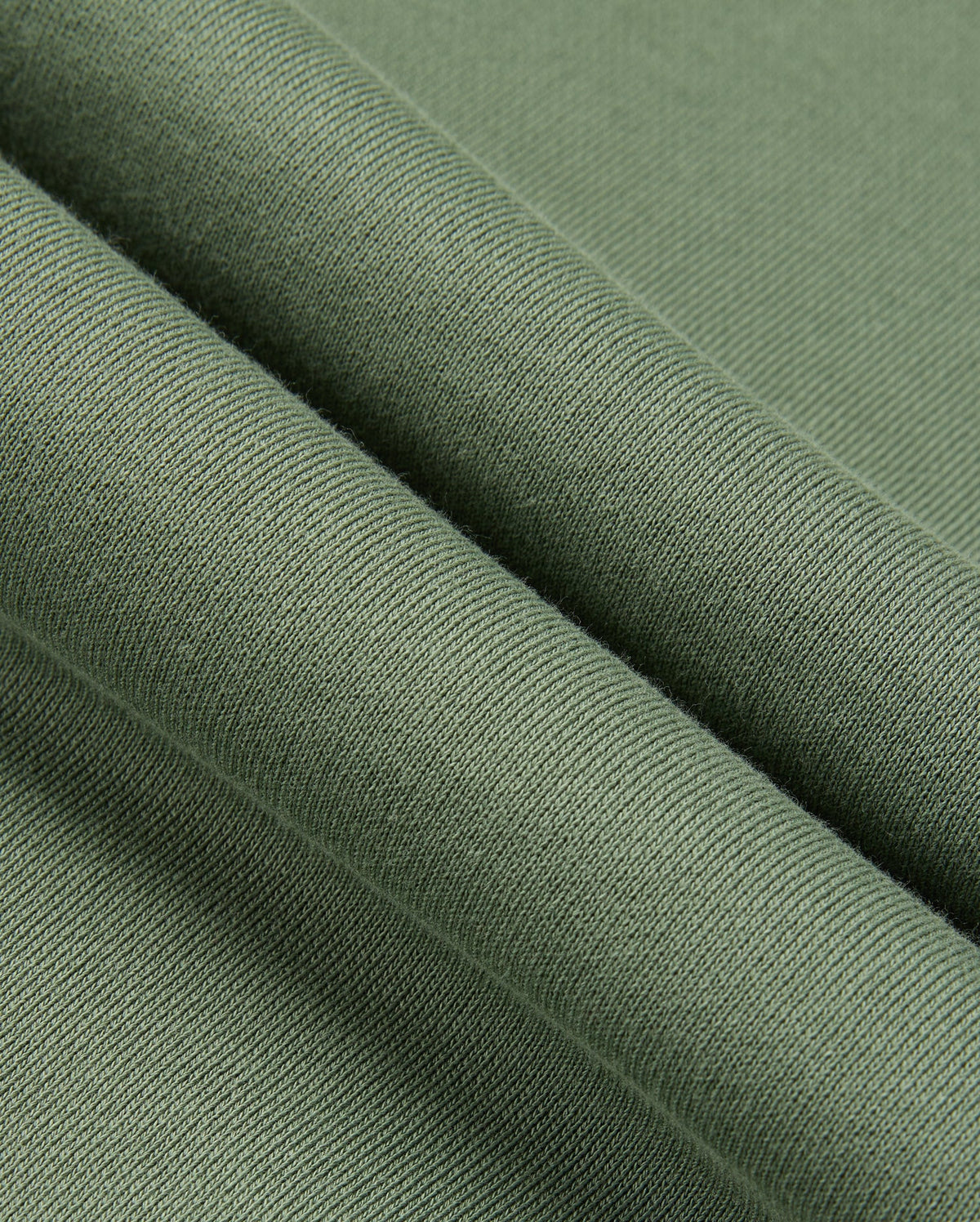 A close-up of the green fabric, resembling the cozy texture of a Psycho Bunny MENS PACIFIC CHENILLE HOODIE (B6H930D200), showcases its smooth feel and fine knitting. The folded fabric highlights its softness and uniform weave, much like luxurious chenille embroidery.