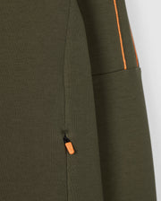 Close-up of the olive green Psycho Bunny Men's Travis Track Jacket (B6J142D200) featuring an orange pull tab on a zippered pocket. Orange stitching detail is visible along a separate seam, contrasting beautifully with the high-quality cotton-blend fabric's texture.