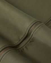 Close-up of a piece of olive green, high-quality cotton-blend fabric showcasing detailed stitching with red thread. The material appears smooth and sturdy, with prominent seams and folds creating subtle shadows and highlights, reminiscent of the craftsmanship found in the Mens Travis Track Jacket (B6J142D200) by Psycho Bunny.
