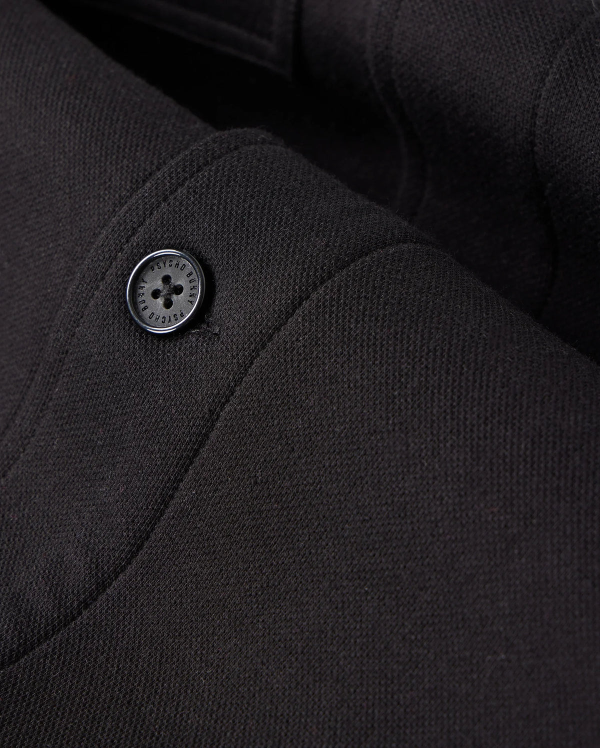 Zoomed-in view of the black fabric from the MENS BEDFORD SHIRT JACKET - B6J290B200 by Psycho Bunny, highlighting the texture and stitching details with a single black button, reminiscent of a work-jacket style.