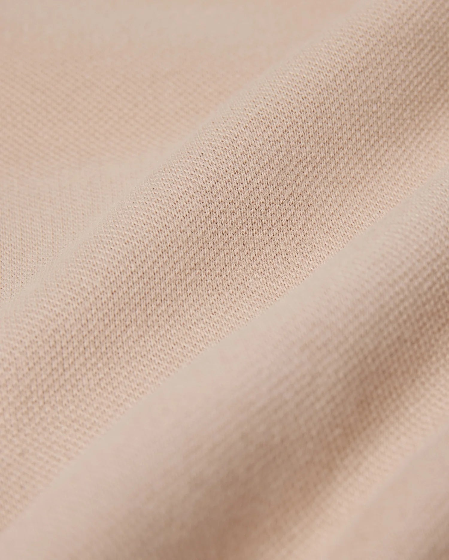 Close-up of a beige fabric featuring a textured, woven surface. The material resembles the fine weave found in the Psycho Bunny MENS BEDFORD SHIRT JACKET - B6J290B200, appearing soft and slightly crumpled, highlighting its smooth texture.