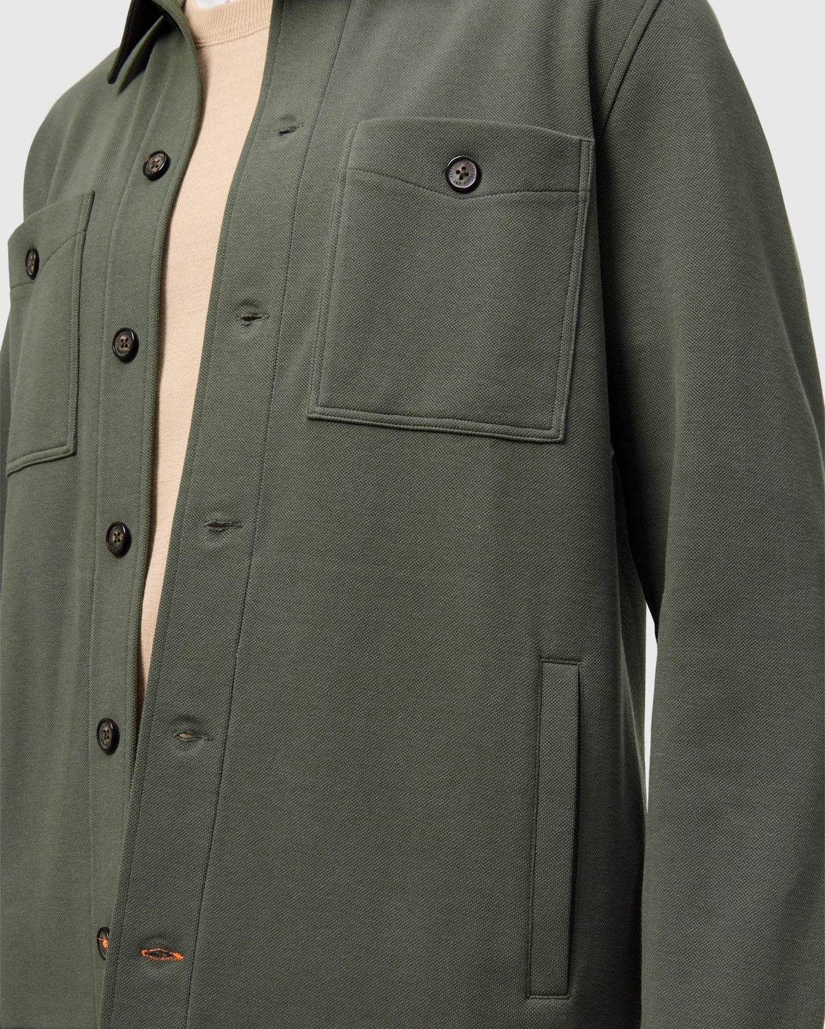 Close-up of a person wearing the Psycho Bunny MENS BEDFORD SHIRT JACKET - B6J290B200 in dark green over a beige shirt. This cotton-blend overshirt, with its urban vibe, showcases two chest pockets and black buttons.
