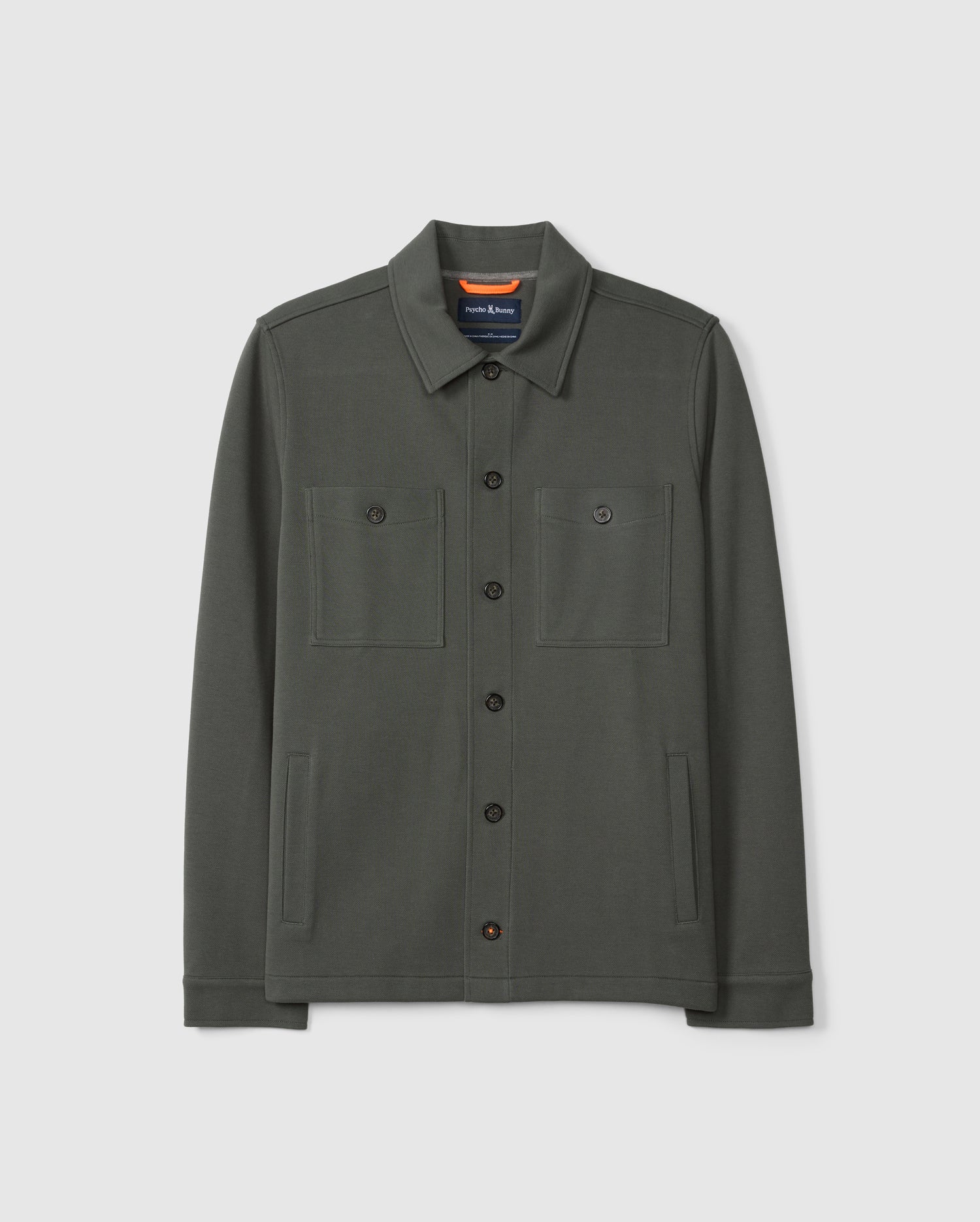 Introducing the MENS BEDFORD SHIRT JACKET - B6J290B200 by Psycho Bunny: a dark green shirt jacket made from a cotton-blend fabric. It includes a collar, two chest pockets, and two side pockets. Its understated design offers a casual and urban look, beautifully showcased against a plain background.