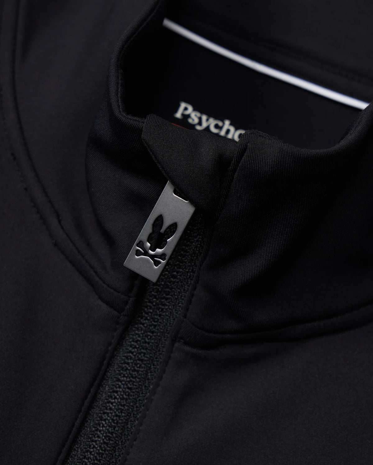 Close-up of the Mens Terrell Sport Zip-Up Jacket in black, featuring a small rabbit logo on the zipper pull. The inside label displays "Psycho Bunny." Made from smooth modal-blend knit, this jacket offers a fitted look with a casual, stylish design ideal for use as a versatile track jacket.