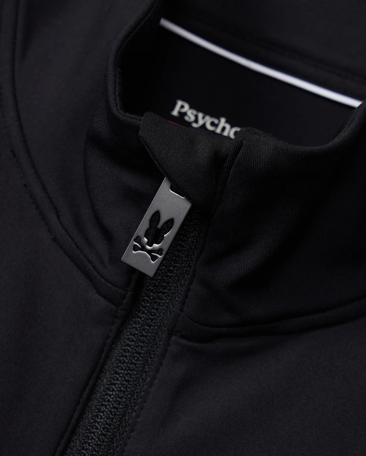 Close-up of the Mens Terrell Sport Zip-Up Jacket in black, featuring a small rabbit logo on the zipper pull. The inside label displays "Psycho Bunny." Made from smooth modal-blend knit, this jacket offers a fitted look with a casual, stylish design ideal for use as a versatile track jacket.