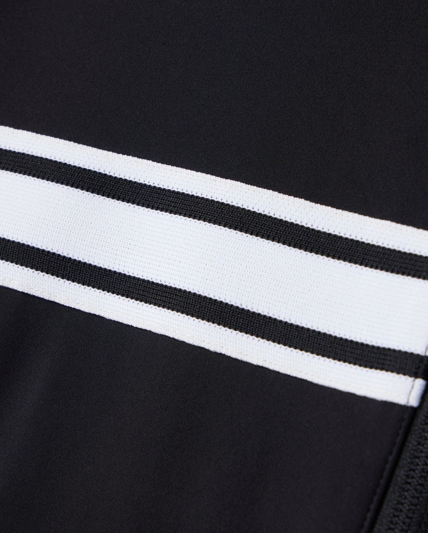 Close-up of the Psycho Bunny MENS TERRELL SPORT ZIP UP JACKET - B6J643C200, featuring a versatile black fabric design with two horizontal white stripes. The smooth and sleek appearance highlights the modal-blend knit texture.