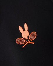 A close-up of a black Psycho Bunny MENS COURTSIDE TRACK JACKET - B6J692C200 featuring an orange embroidered design of a bunny head above two crossed tennis rackets.