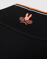 Close-up of a Psycho Bunny MENS COURTSIDE TRACK JACKET - B6J692C200 made from stretch cotton-blend jersey, featuring a logo with a red silhouette of a rabbit's head above two crossed red tennis rackets. The garment has a thin red, white, and black striped band near the top edge and logo-engraved hardware.