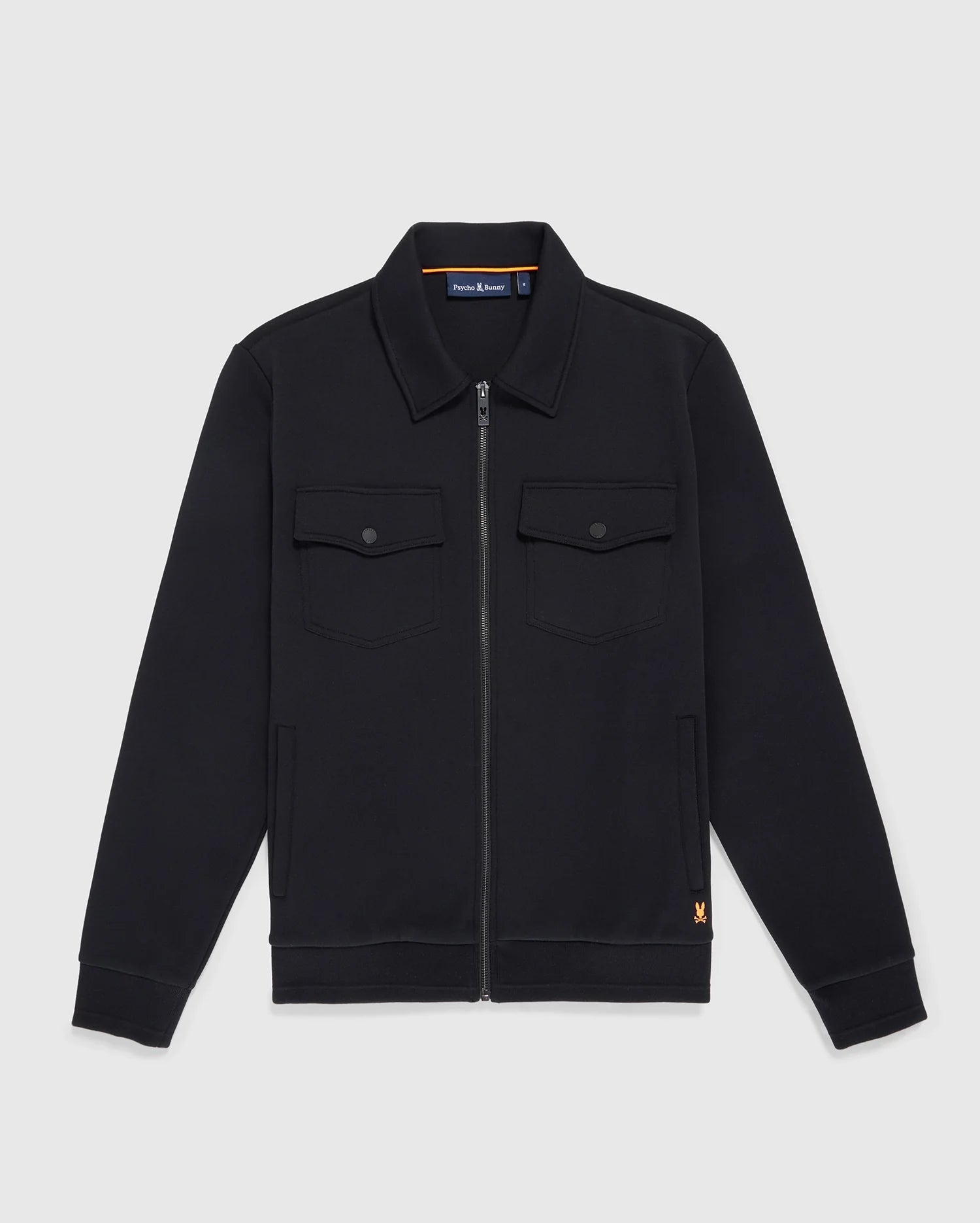 The MENS OROVILLE BOMBER JACKET - B6J712A200 from Psycho Bunny is a black zip-up cotton-poly jacket with a collar and long sleeves. This outerwear includes two buttoned chest pockets and showcases a small orange logo near the hem, set against a plain white background.