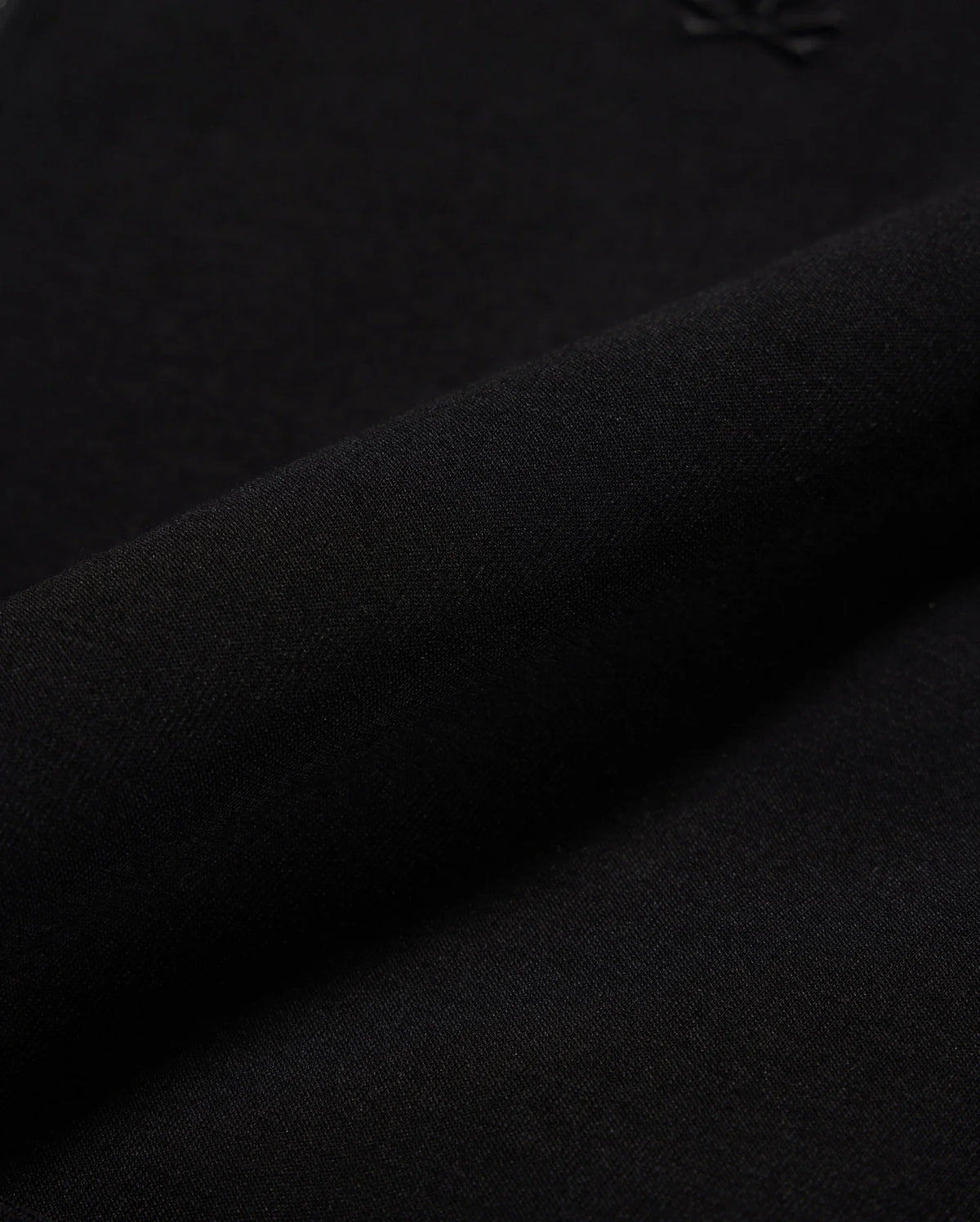 Close-up of the MENS OROVILLE BOMBER JACKET - B6J712A200 by Psycho Bunny, made from black cotton-poly fabric. The fabric is smooth and tightly woven with a subtle shine, perfect for outerwear. It appears soft and flexible, with a small embossed logo visible in the top right corner, making it ideal for crafting stylish bomber jackets that offer both elegance and comfort.