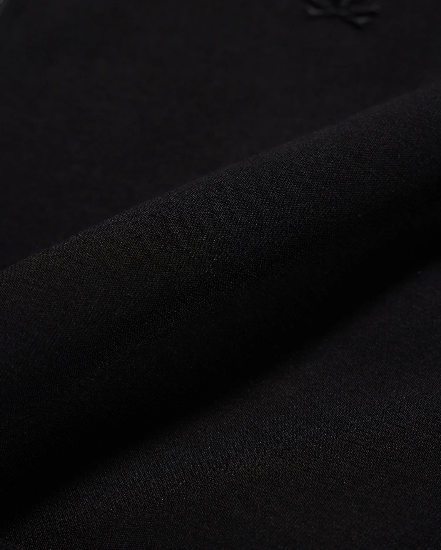 Close-up of the MENS OROVILLE BOMBER JACKET - B6J712A200 by Psycho Bunny, made from black cotton-poly fabric. The fabric is smooth and tightly woven with a subtle shine, perfect for outerwear. It appears soft and flexible, with a small embossed logo visible in the top right corner, making it ideal for crafting stylish bomber jackets that offer both elegance and comfort.