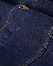 The MENS PATHE DENIM JACKET - B6J741X1CO by Psycho Bunny features a close-up view of dark blue denim with an apparent pocket and button. The orange stitching contrasts with the fabric, and embroidered details enhance the texture, creating a striking appearance.