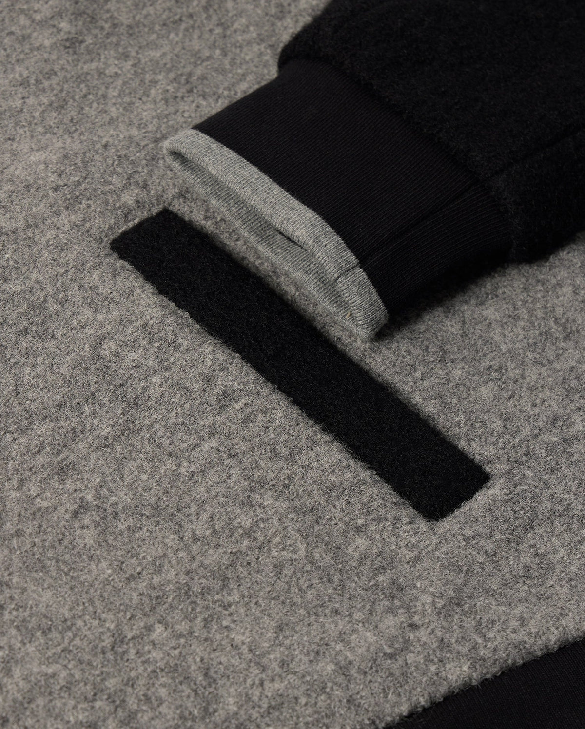 A close-up of Psycho Bunny's MENS TOM WOOL BOMBER JACKET - B6J744D200 reveals its sophisticated gray wool design, highlighted by a black cuff. This elegant jacket boasts a luxurious black and gray striped lining peeking through the sleeve, along with a distinctive black rectangular pocket flap on the body. Its texture is soft and plush.