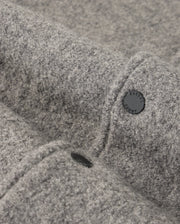 Close-up of a grey woolen fabric with a textured surface reminiscent of the MENS TOM WOOL BOMBER JACKET - B6J744D200 by Psycho Bunny. The fabric is adorned with a black button embossed with text, which provides a subtle contrast against the soft material.