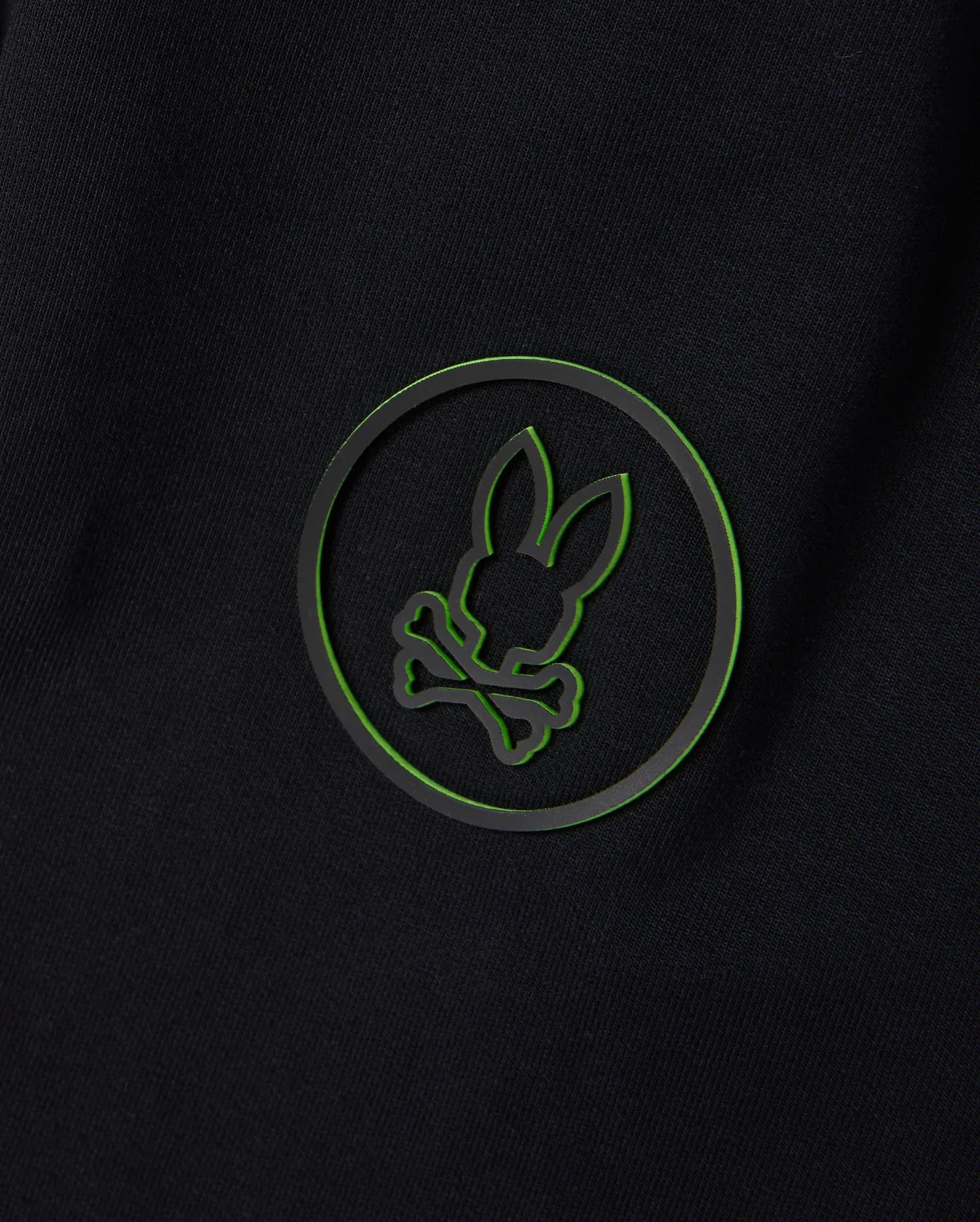 The edgy and modern design of a black background with a green outlined circle featuring a silhouette of bunny ears and crossbones pairs perfectly with the versatile style of the Psycho Bunny MENS MYKEL MIXED MEDIA JACKET - B6J875D200.