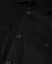 The Psycho Bunny Men's Hillcrest Padded Shacket (B6J936D200) features a black fabric with a collar, buttoned front, and two chest flap pockets with buttons. The neon lining adds vibrancy, while the textured fabric and detailed stitching are prominently showcased.