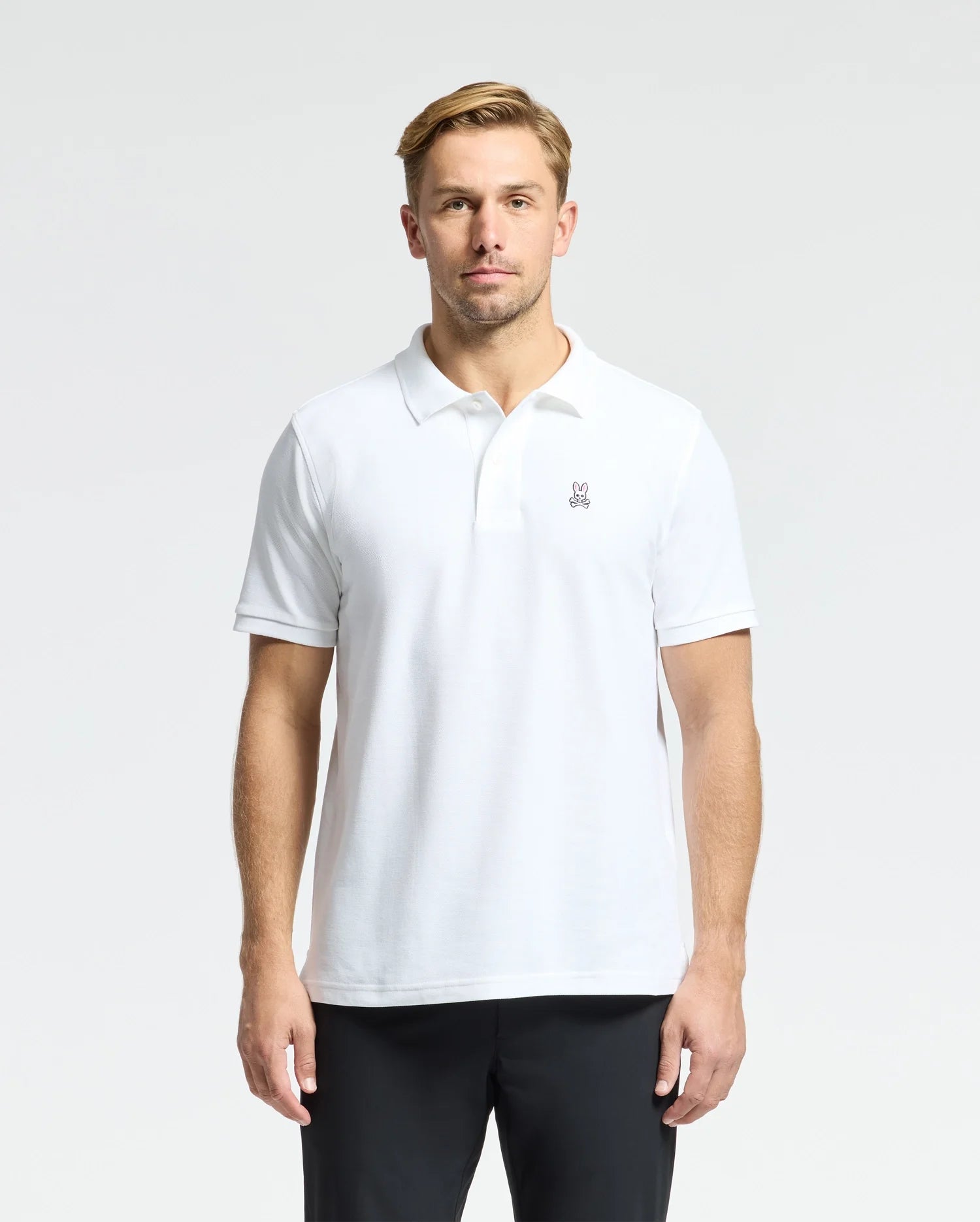 A man in a MENS CLASSIC PIQUE POLO SHIRT by Psycho Bunny, made from 100% Pima cotton and featuring mother-of-pearl buttons, stands against a plain background. His hands rest casually at his sides, and he wears a neutral expression.
