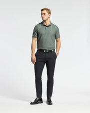 A man stands wearing the Psycho Bunny MENS CLASSIC PIQUE POLO SHIRT - B6K001B200, crafted from Pima cotton and showcasing the embroidered Bunny logo. He pairs it with black pants and shoes. With short hair, glasses, and a watch on his left wrist, he poses against a plain white background.